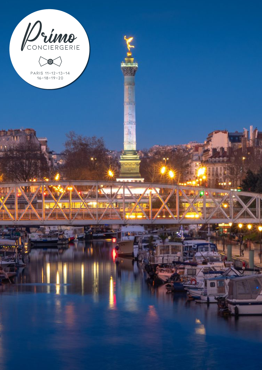 Vue nocturne de la Colonne de Juillet sur la place de la Bastille, éclairée et entourée de bateaux sur le canal.