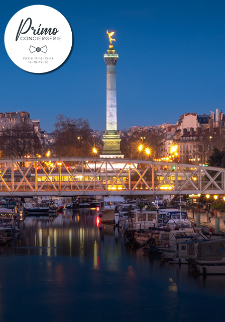 Vue nocturne de la Colonne de Juillet sur la place de la Bastille, éclairée et entourée de bateaux sur le canal.